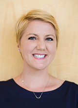 Woman with short blonde hair wearing a navy top and necklace