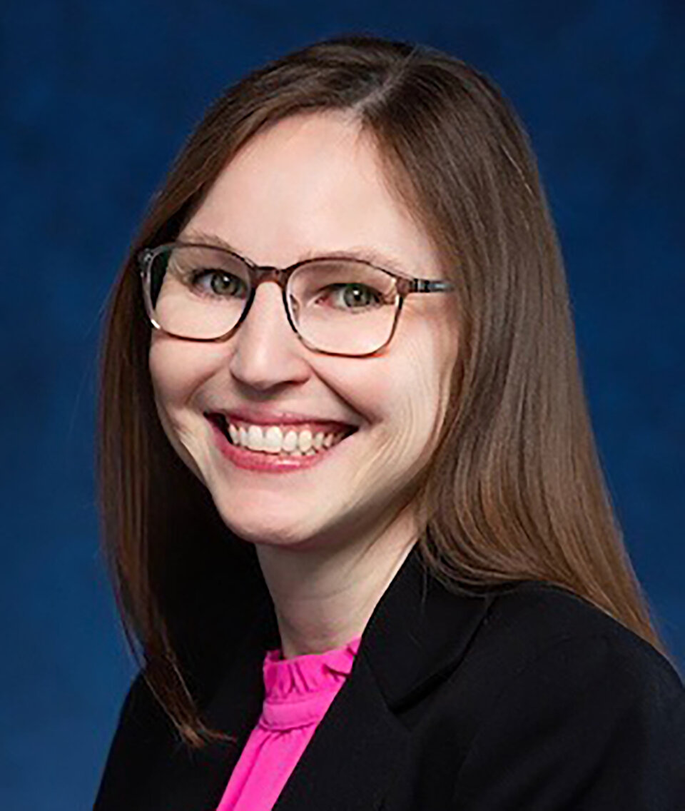 Woman with glasses, long brown hair, pink blouse, and black blazer 